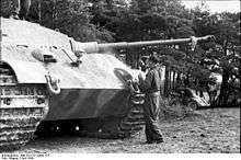 A man working at the front of a large tank, it's hull taller than the top of his head
