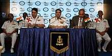 Uniformed man at a table, flanked by two other men