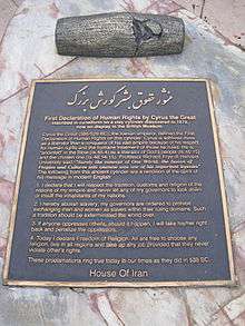 Monument consisting of a bronze plaque fixed to a sloping marble slab, with a bronze replica of the Cyrus Cylinder above the plaque.