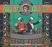 Two men with skull heads, in formal attire, operate mechanical devices. In the foreground is the Wall of Sound concert sound system, and roses.