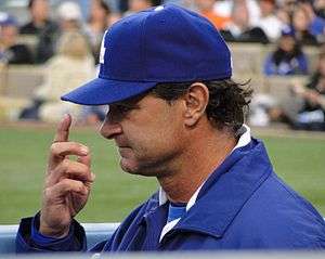 A profile view of a light-skinned man in a blue baseball cap, reading "LA" in interlocked white letters, and a blue jacket with a white stripe on the collar pointing to his cap.