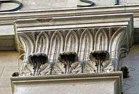 A square carved stone capital with two different types of leaves going up and around to the top