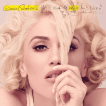 Stefani's face is shown while she pulls a lock of hair down in front of her face with her finger.