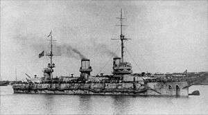 A grey ship with two masts, two funnels and draped with nets above the waterline