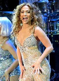 A brunette woman with a head set microphone, wearing a metallic outfit.