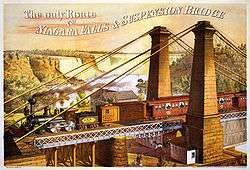 A train crosses the top of the double-deck bridge. In the background is a waterfall.