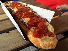 A typical zapiekanka with mushrooms under melted cheese smeared with kethup, served on a paper tray