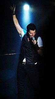 Singer in spotlight, left hand holding microphone and right arm raised