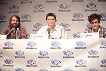 Three men sit at a table at a convention.